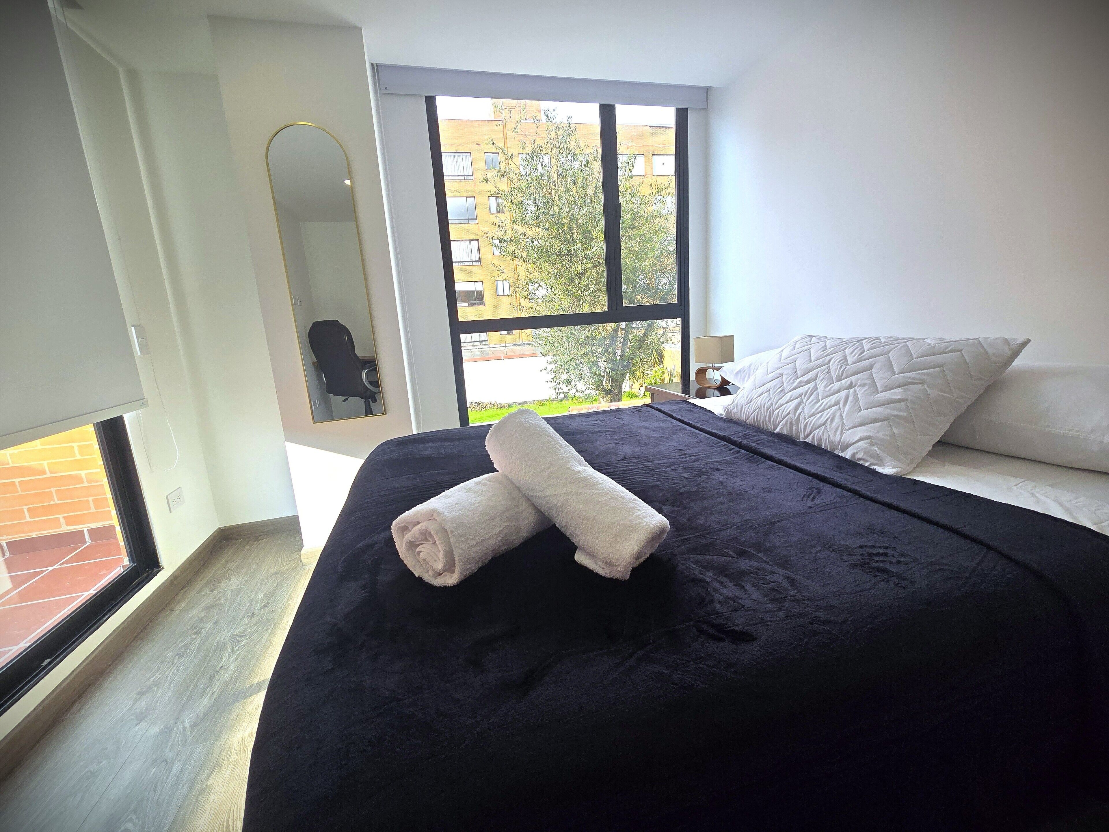 A bedroom with a large bed, a window with a view of buildings, and a door leading to an outdoor area.