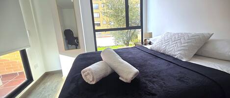 Un dormitorio con una cama grande, una ventana con vistas a edificios y una puerta que da a un espacio exterior.