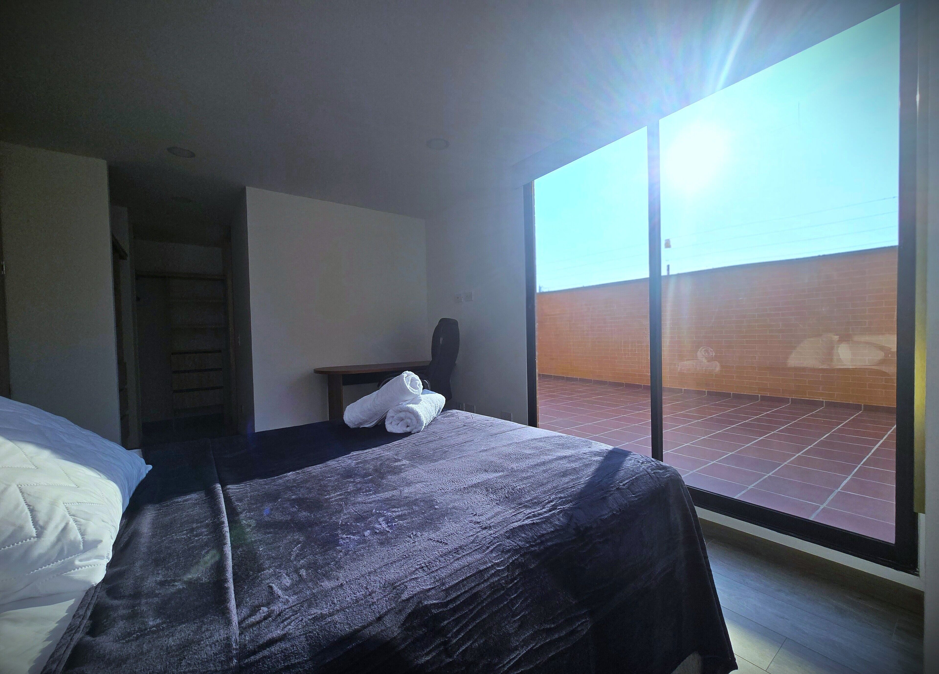 A hotel room with a bed, a chair, a table, and a view of a brick wall through a large window.