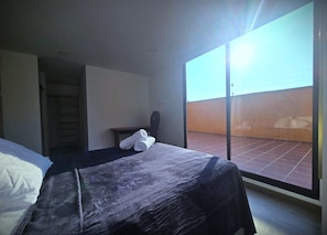 Ein Hotelzimmer mit Bett, Stuhl, Tisch und Blick auf eine Ziegelwand durch ein großes Fenster.