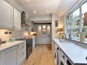 A modern kitchen with a built-in oven, a washing machine, and a window with a view of greenery. - Luxury Stone Painswick Retreat for 6 (Stroud)