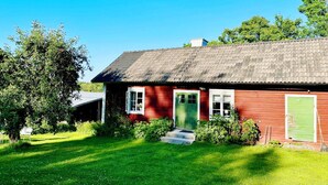 A red wooden house with a green door and windows, surrounded by a well-maintained lawn and trees. - 4 Star Holiday Home in Osthammar (Osthammar)
