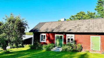 A red wooden house with a green door, white windows, and a sloped roof.