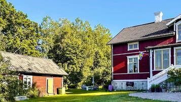 A red house with a white porch and a small shed with a thatched roof.