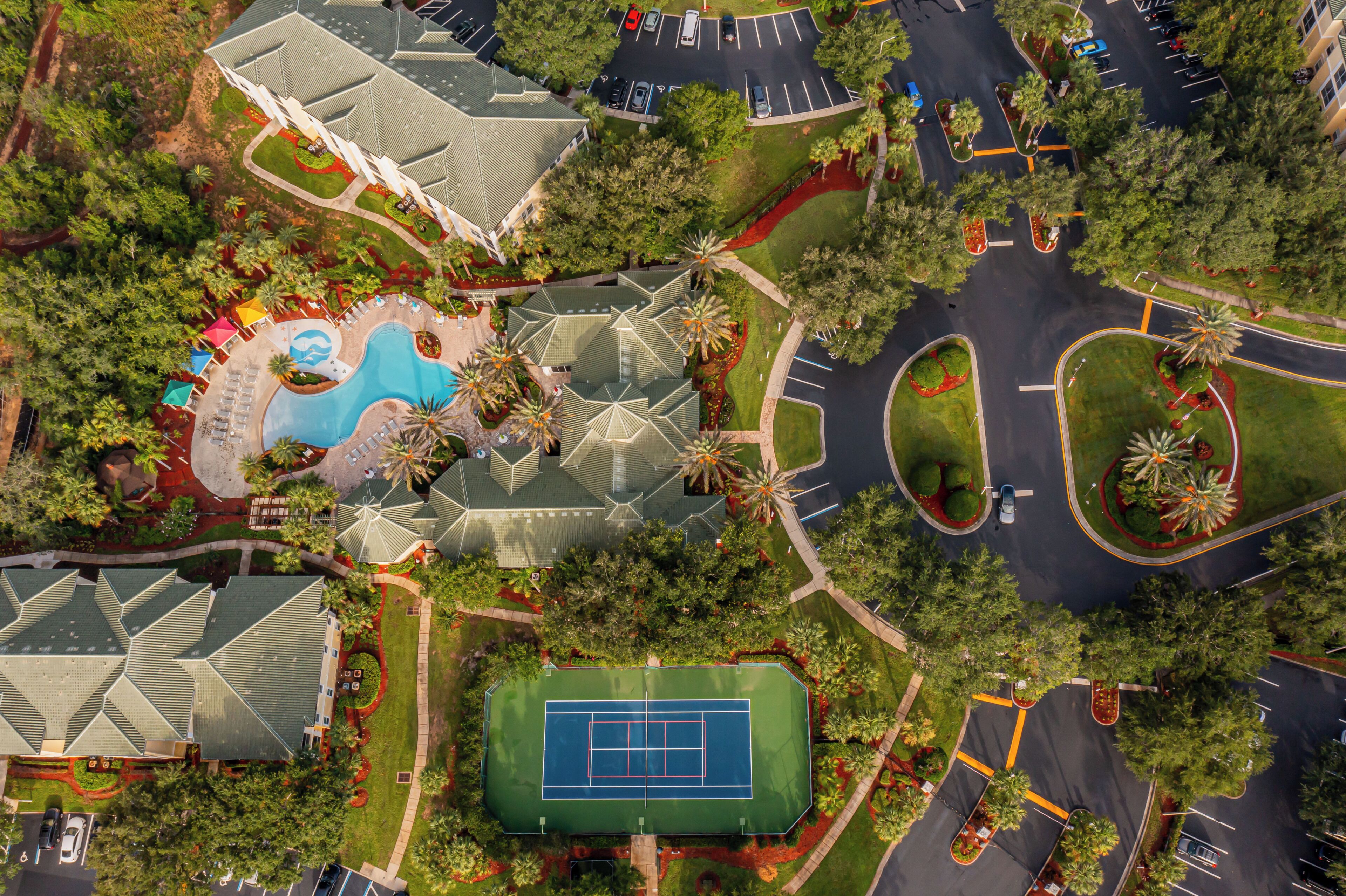Vue aérienne d’un complexe hôtelier doté d’une piscine, d’un court de tennis et d’espaces paysagers.