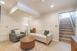 Ein Wohnzimmer mit Sofa, Sessel, Couchtisch und einer Treppe.