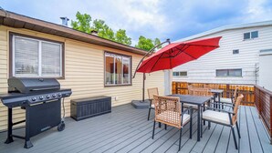 Une terrasse avec un barbecue, du mobilier d’extérieur et un parasol rouge.