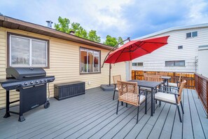 Eine Terrasse mit Grill, Gartenmöbeln und einem roten Sonnenschirm.