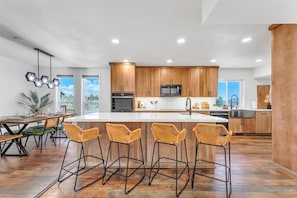 A modern kitchen with wooden cabinets, a central island, and bar stools. - Reno Retreat - 3BR Oasis w Swim Spa, Hot Tub (Reno)