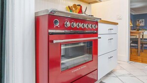 En rød Fisher & Paykel ovn i et køkken med hvide skabe og klinkegulv.