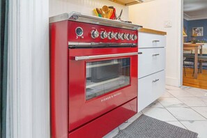 A red Fisher & Paykel oven in a kitchen with white cabinets and a tiled floor. - The Luxury Brick Home Mature Yard Chef Kitchen (Reno)