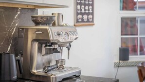En kaffemaskine med digitalt display, en elkedel og en kaffekop på en bordplade.