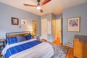 A bedroom with a bed, a ceiling fan, a bedside table, a nightstand, a lamp, a framed picture, a door, and a dresser. - The Luxury Brick Home Mature Yard Chef Kitchen (Reno)