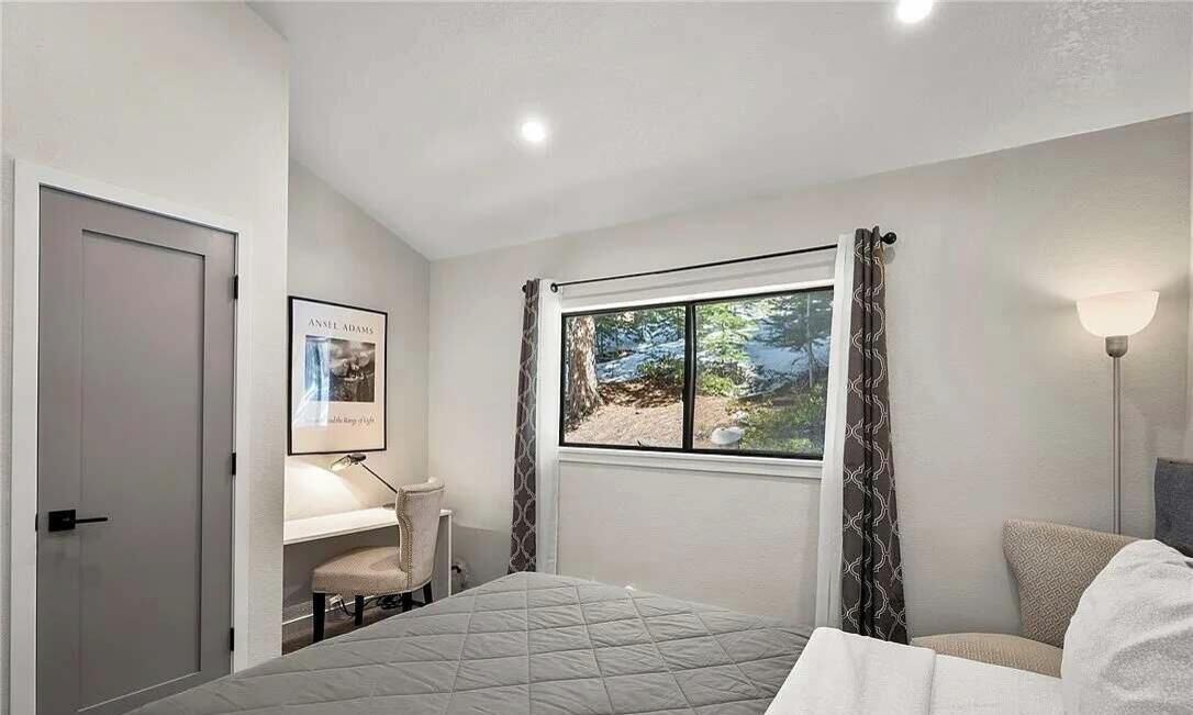 A bedroom with a bed, a desk, a chair, a window with curtains, and a lamp.