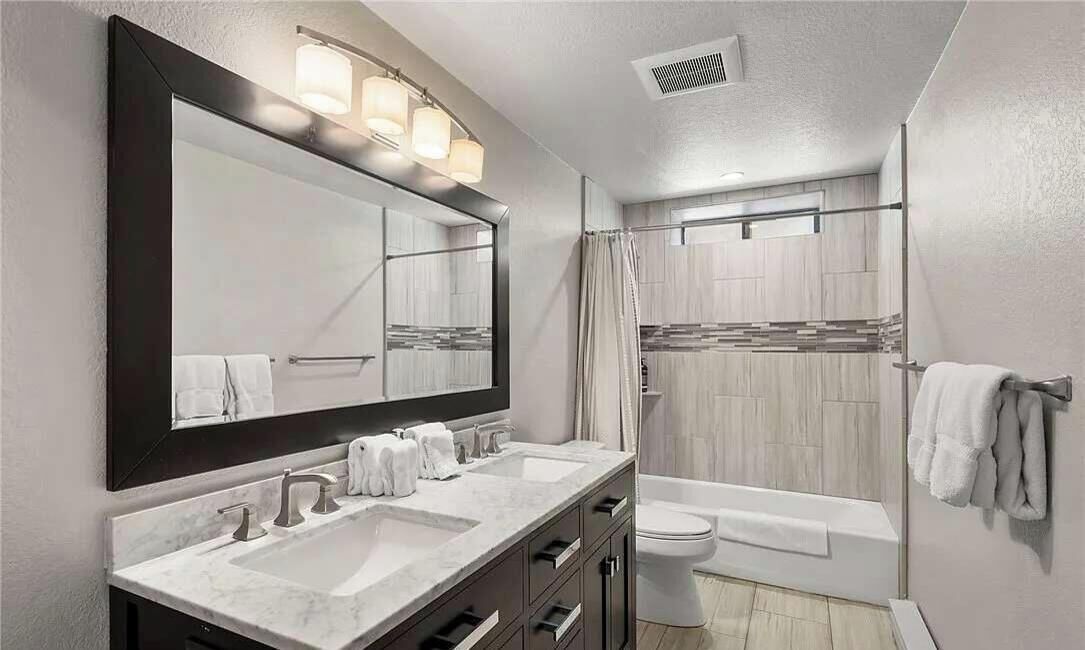 A modern bathroom with a large mirror, dual sinks, a toilet, and a bathtub.