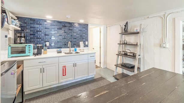 Een keuken met een blauwe betegelde achterwand, witte kastjes, een broodrooster en een koffiezetapparaat.