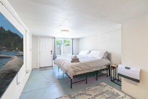 A bedroom with a bed, a bedside table, a wall-mounted heater, and a view of the outdoors. - Cozy Reno Studio Near Hot Spots (Reno)