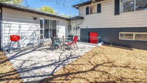 A house with a patio area featuring a table and chairs, a red door, and a garage. - Spacious Pet-friendly Retreat 4br, Grill, 5 Beds (Reno)