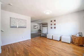 A spacious room with hardwood flooring, a white sofa set, a wooden cabinet, and wall-mounted pictures. - Spacious Pet-friendly Retreat 4br, Grill, 5 Beds (Reno)