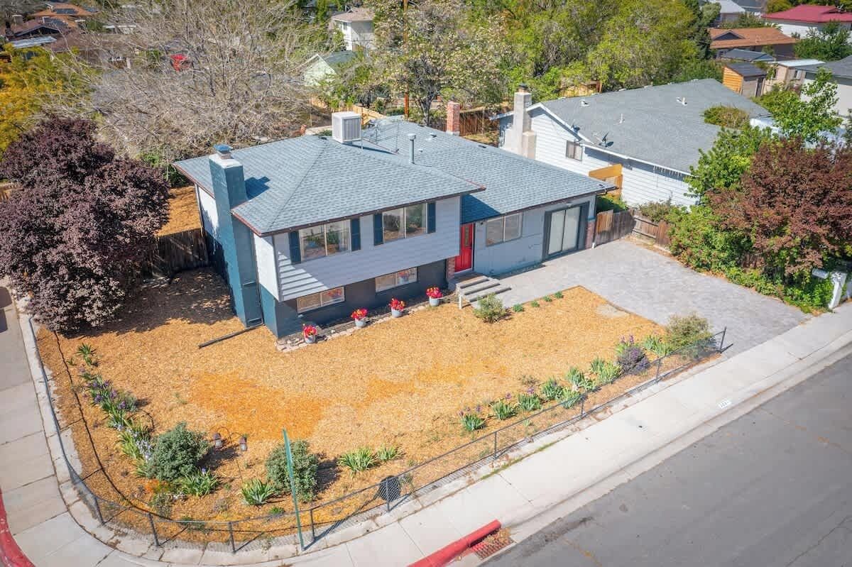 A two-story house with a sloped roof, a red door, and a small front yard with a gravel path and potted plants.