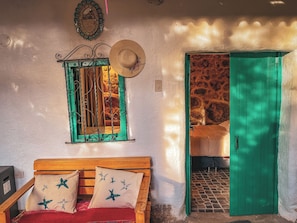 A room with a wooden bed, a green door, a window with green frames, and a wall-mounted mirror.