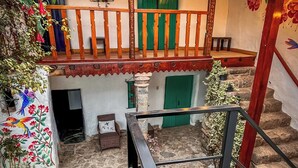A covered outdoor area with a wooden balcony, stone flooring, and green doors.