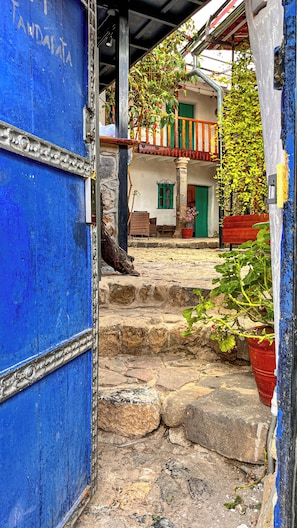 A stone staircase leading to a building with a blue door, a balcony with plants, and a red bench. - Heyyy Cusco (Cusco)
