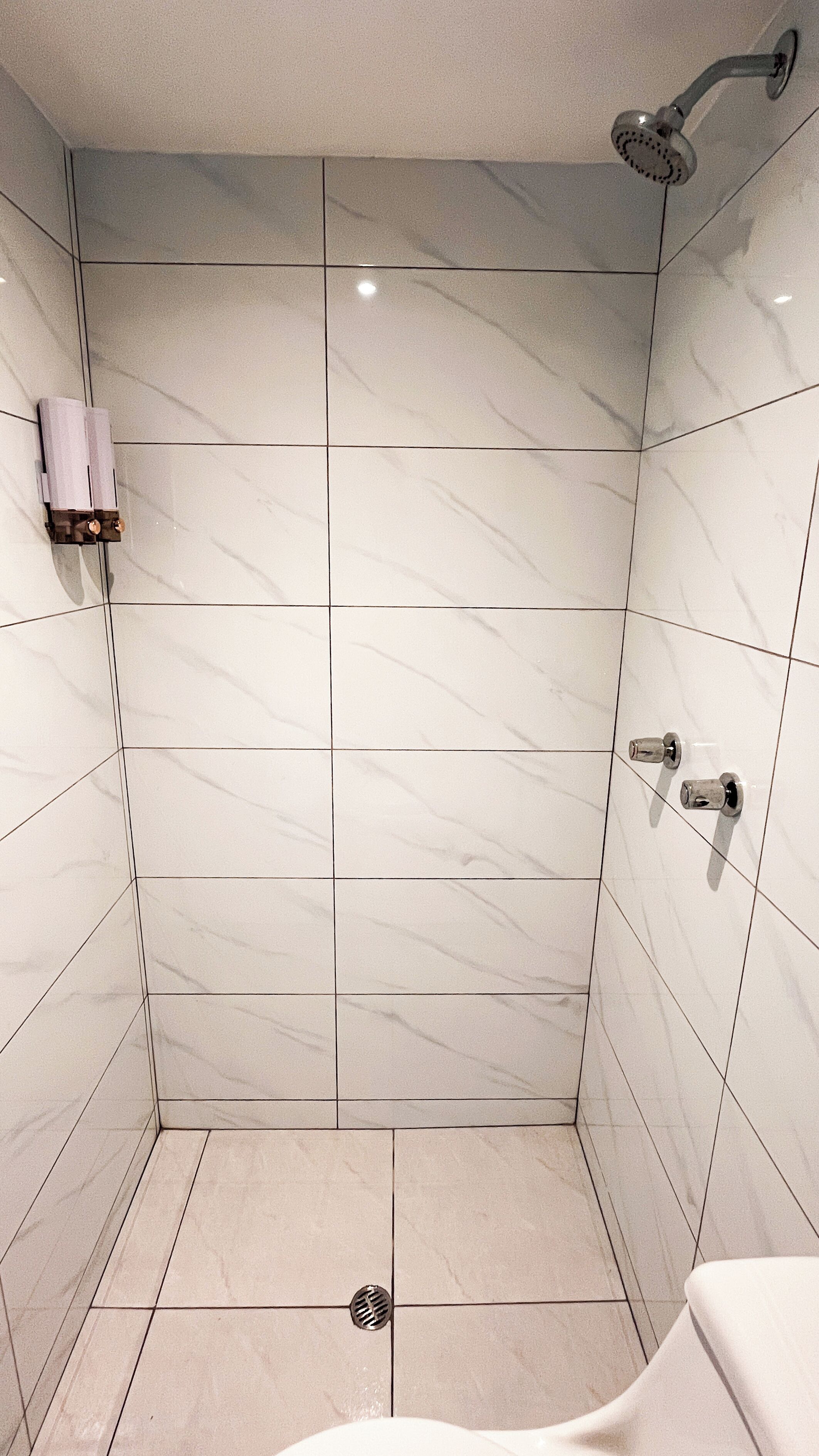 Un baño con baldosas de mármol blanco, una ducha con cabezal de ducha manual y un inodoro.