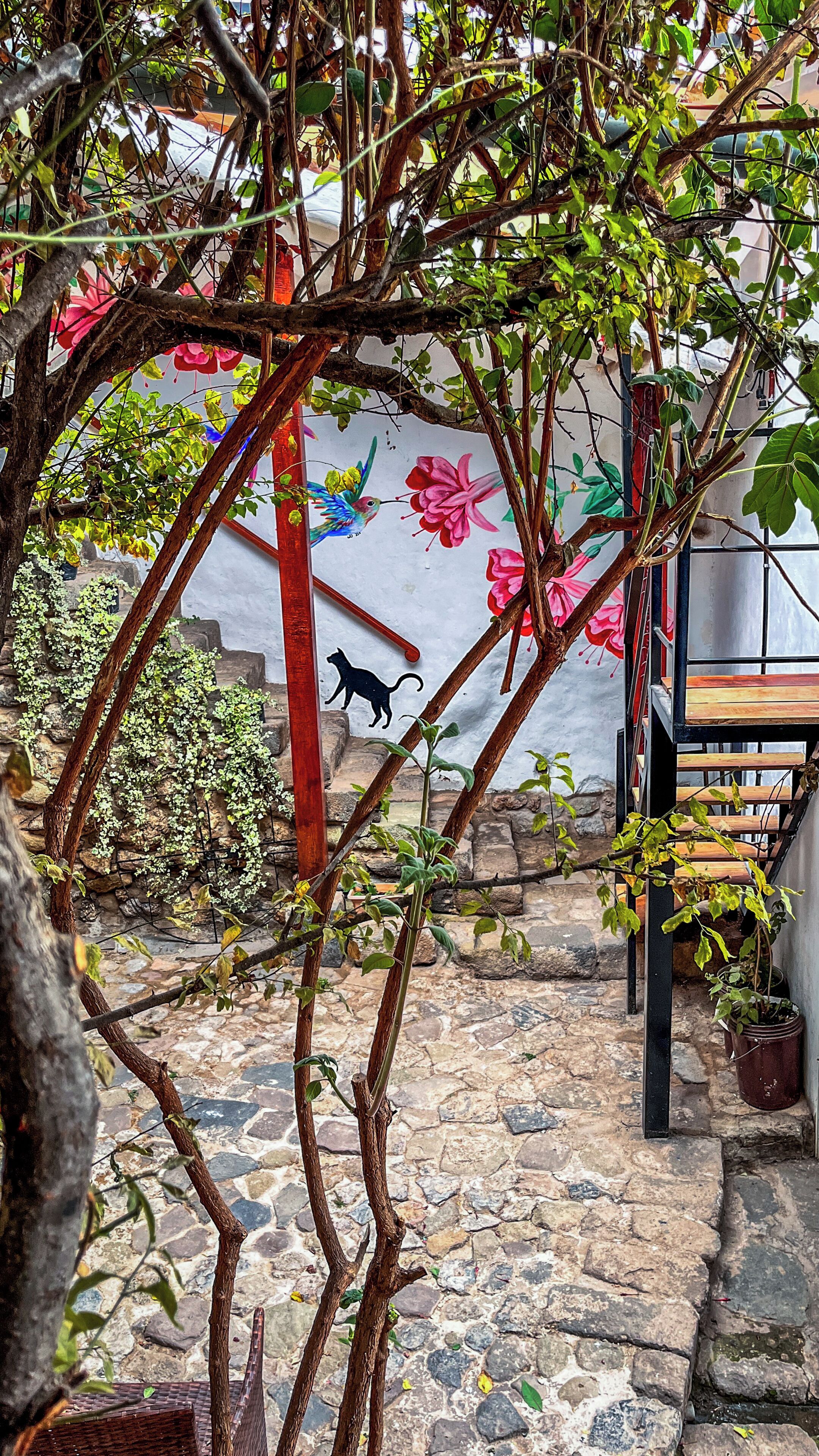 Un sendero empedrado que lleva a un banco de madera y un mural con motivos florales y de animales.