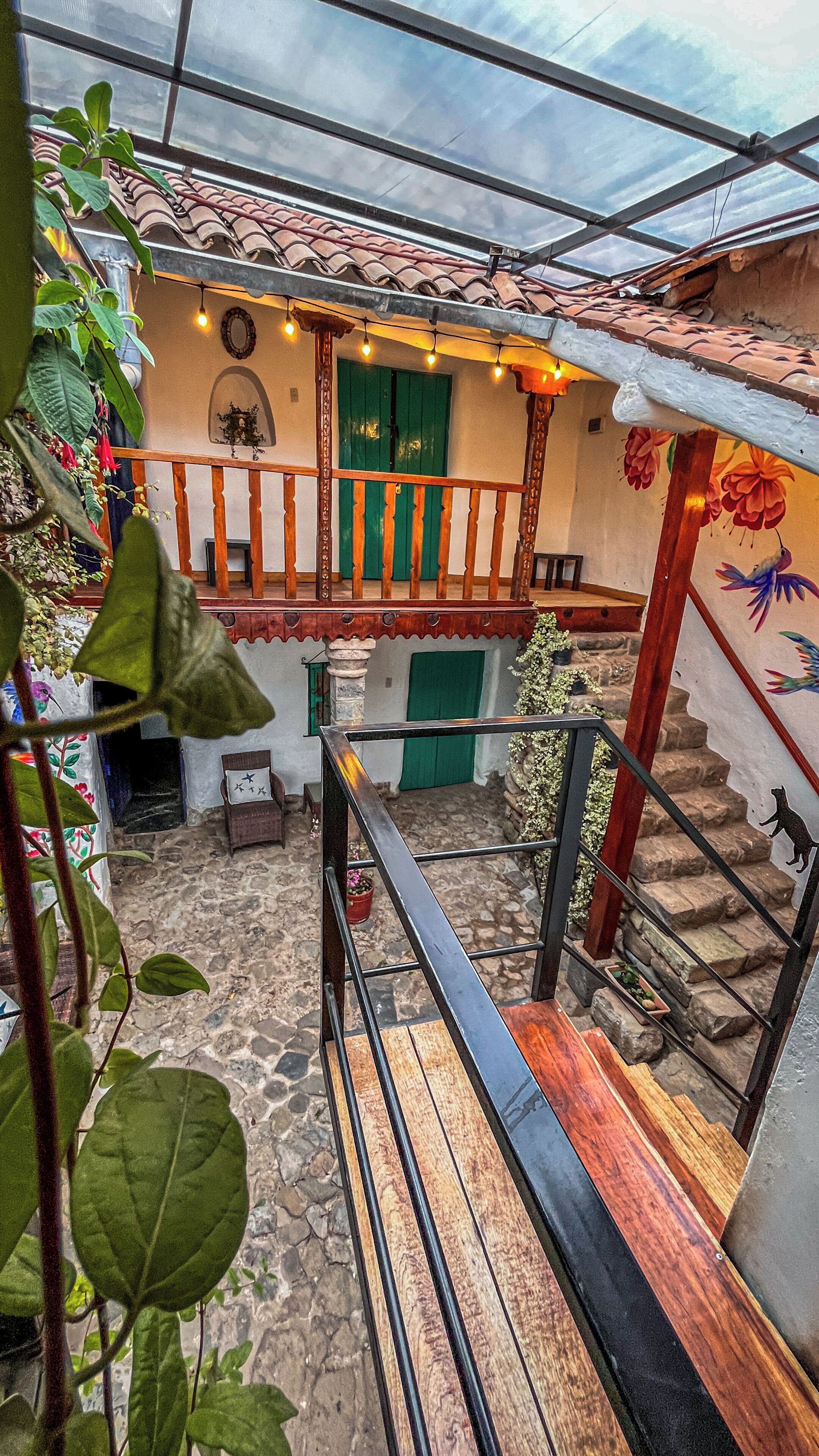 A covered outdoor area with a wooden staircase, a green door, and a stone floor.