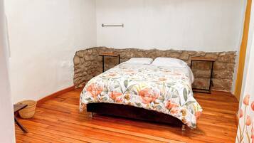 A bedroom with a wooden floor, a bed with a floral bedspread, a stone wall, and a metal headboard.