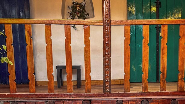A wooden balcony with a railing, a small table, and a potted plant.