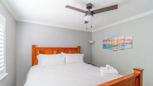 A neatly made bed with a wooden headboard, a ceiling fan, and a wall with a series of paintings. - Modern Getaway for 11- Hot Tub, Games, Gym (Reno)