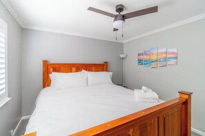 Ein ordentlich bezogenes Bett mit einem Holzkopfstück, einem Deckenventilator und einer Wand mit einer Reihe von Bildern.