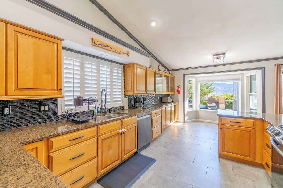 A kitchen with wooden cabinets, granite countertops, and a view to the outside.