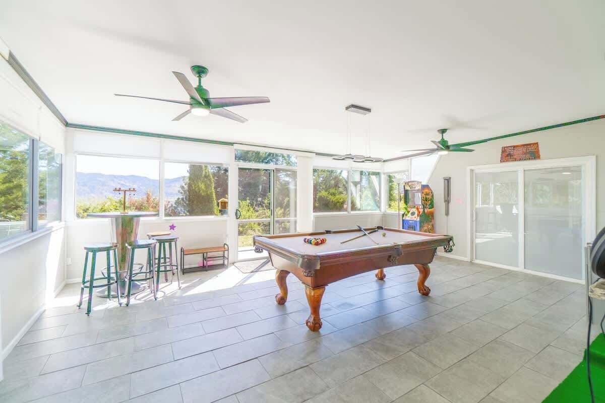 A pool table in a bright room with large windows, ceiling fans, and a view of the outdoors.