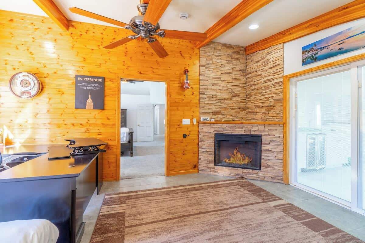 Un interno in legno con camino, una ventola a soffitto e vista attraverso una porta vetrata.