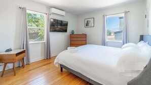 Un dormitorio con cama, escritorio, cómoda y ventana con cortinas.