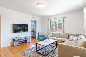 A living room with a sofa, coffee table, TV, and a view of a cityscape through a window. - Midtown Sanctuary w Pac-man! (Reno)
