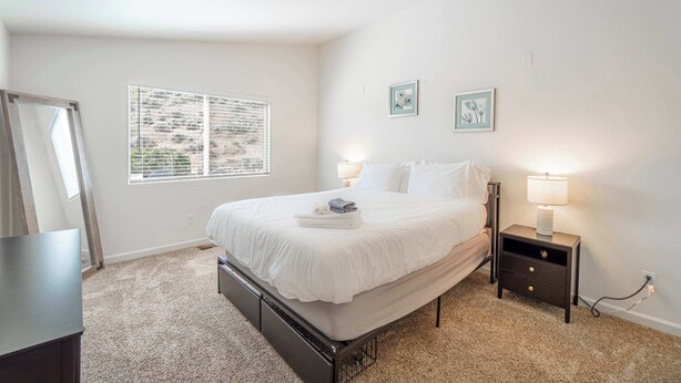 A bedroom with a bed, bedside table, lamp, and window with blinds. - Large Group Escape, 5 Beds, Pets Welcome (Reno)