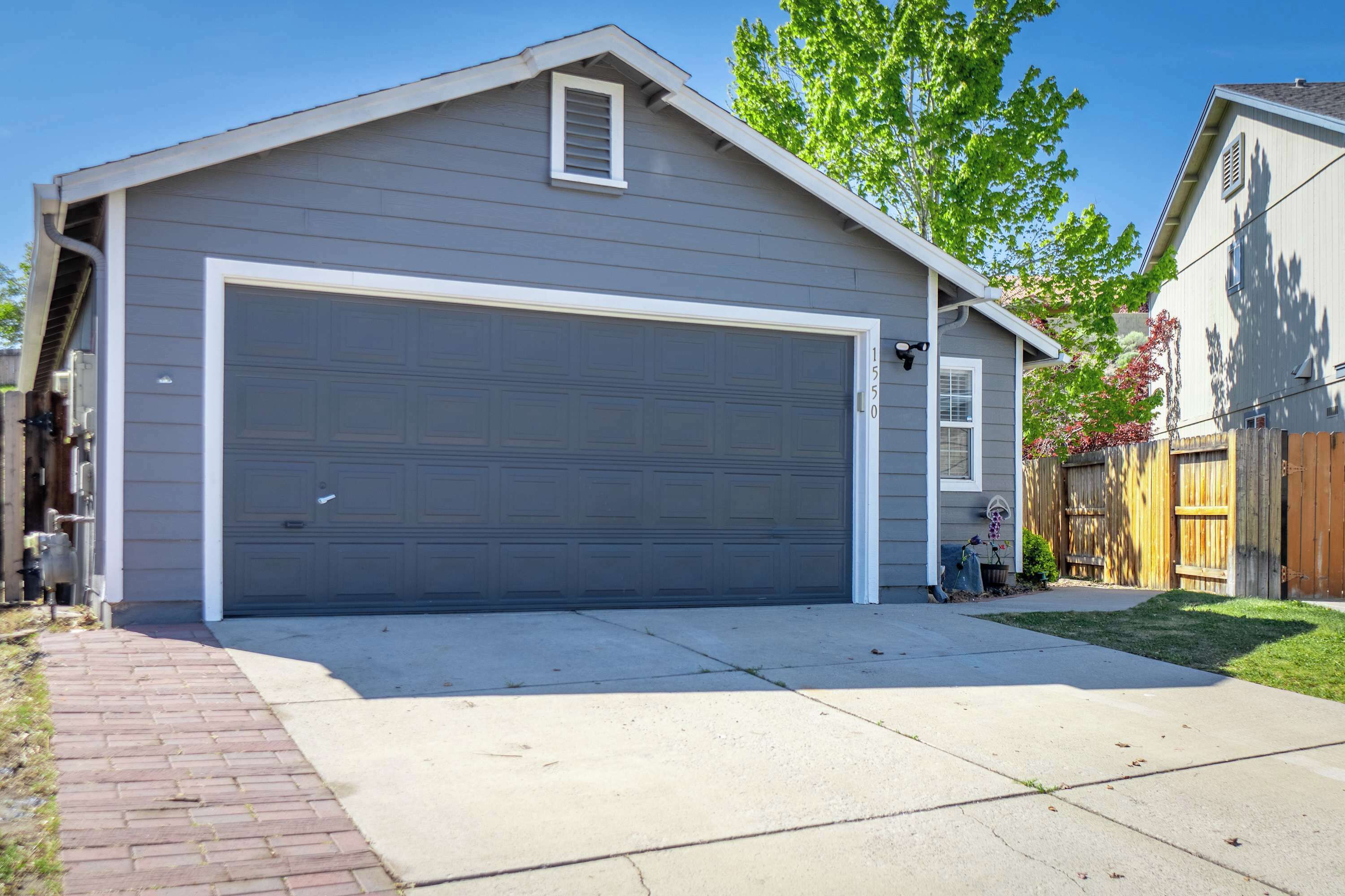 A single-story house with a large garage door, a brick driveway, and a wooden fence.