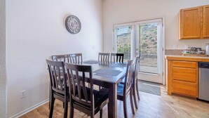 A dining area with a table and chairs, a clock on the wall, a kitchen with wooden cabinets, and a door leading outside. - Large Group Escape, 5 Beds, Pets Welcome (Reno)