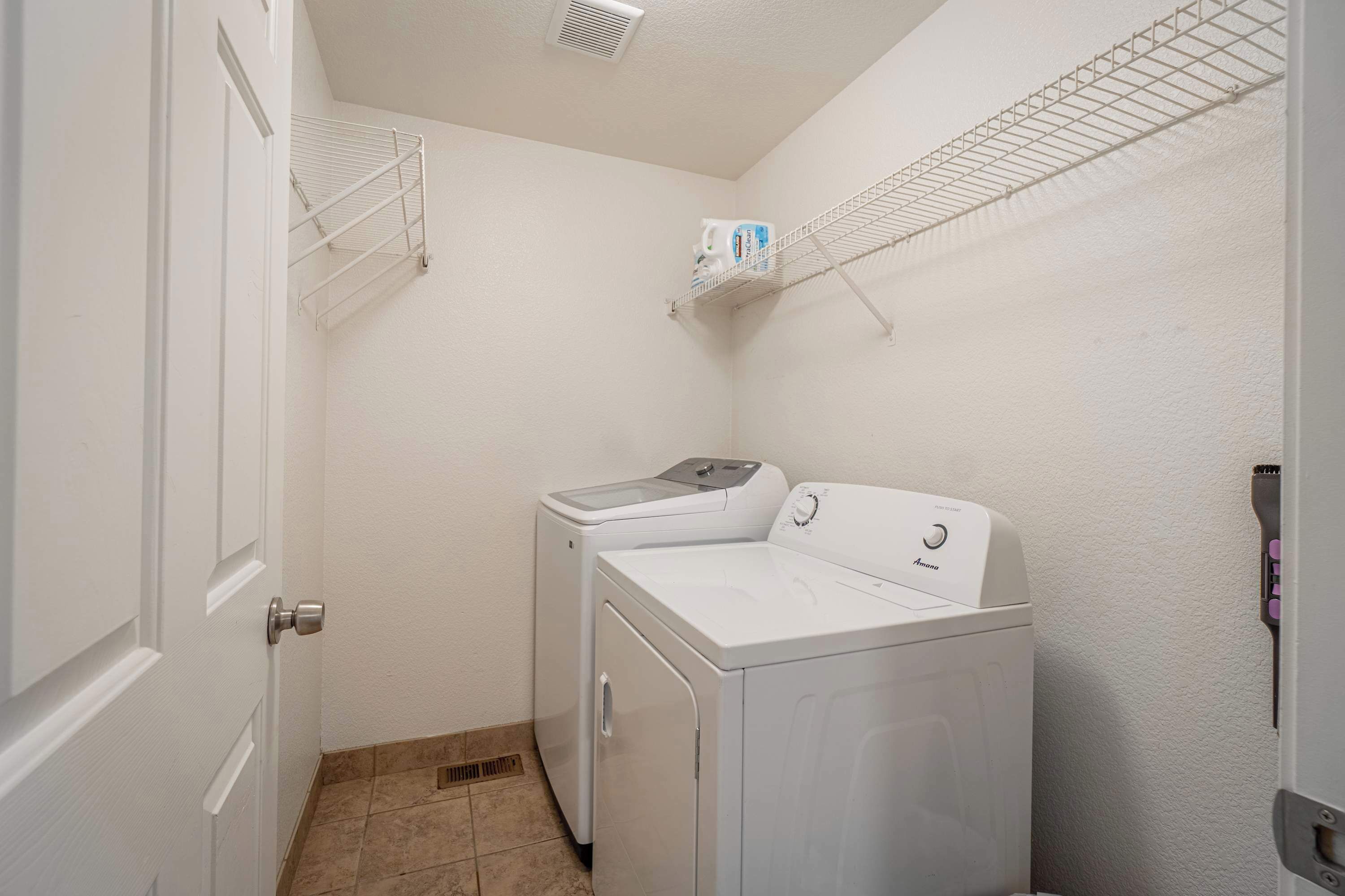A laundry room with a washer and dryer, metal shelves, and a door.