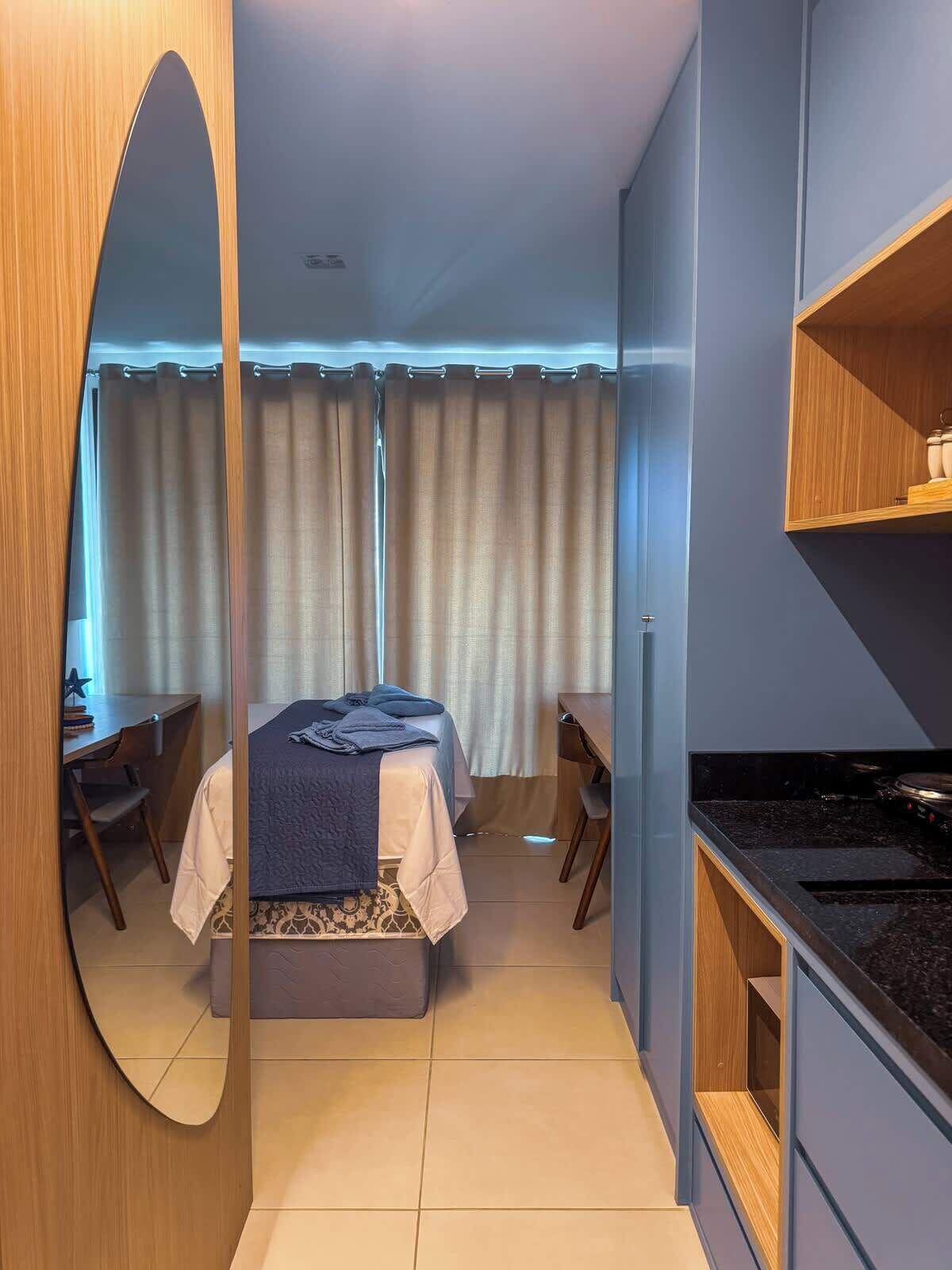 Une chambre d’hôtel de taille réduite, comprenant un lit, un bureau, une chaise et une kitchenette.