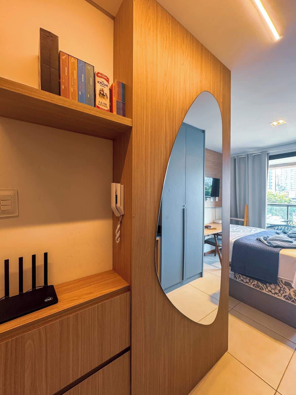 Une chambre d’hôtel avec une armoire en bois, une table de chevet avec un téléphone, un miroir, un lit recouvert d’une courtepointe bleue et une vue sur l’extérieur.