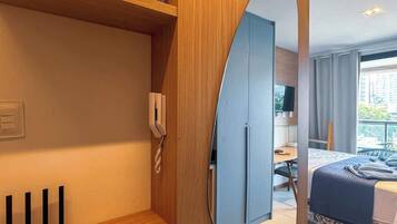 Une chambre d’hôtel avec une armoire en bois, une table de chevet avec un téléphone, un miroir, un lit recouvert d’une courtepointe bleue et une vue sur l’extérieur.
