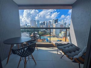 A balcony with a table and chairs, a sofa, and a city view. - Próximo ao farol, 400m da praia, varanda & rooftop (Salvador)