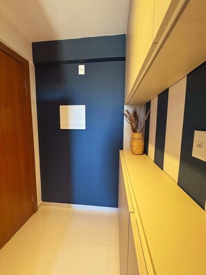 A hallway with a dark blue wall, a wooden door, and a yellow bench with a basket on it. - Studio c/ Varanda Vista Mar • Stella Maris & Farol (Salvador)