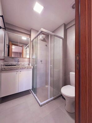 Ein modernes Badezimmer mit einer gläsernen Dusche, einer weißen Toilette und einer Arbeitsplatte aus Granit.