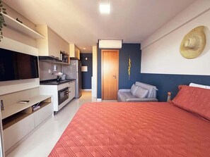 Ein modernes Schlafzimmer mit einem großen Bett, einem Fernseher, einer Küchenzeile und einer Tür zu einem anderen Raum.